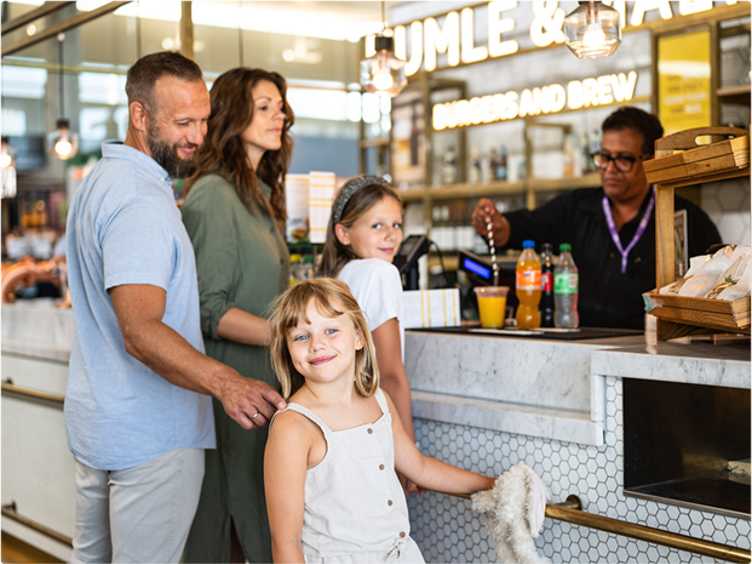 Familie som bestiller mat ved en restaurantdisk mens en kasserer hjelper til i en moderne og lys spisemiljø