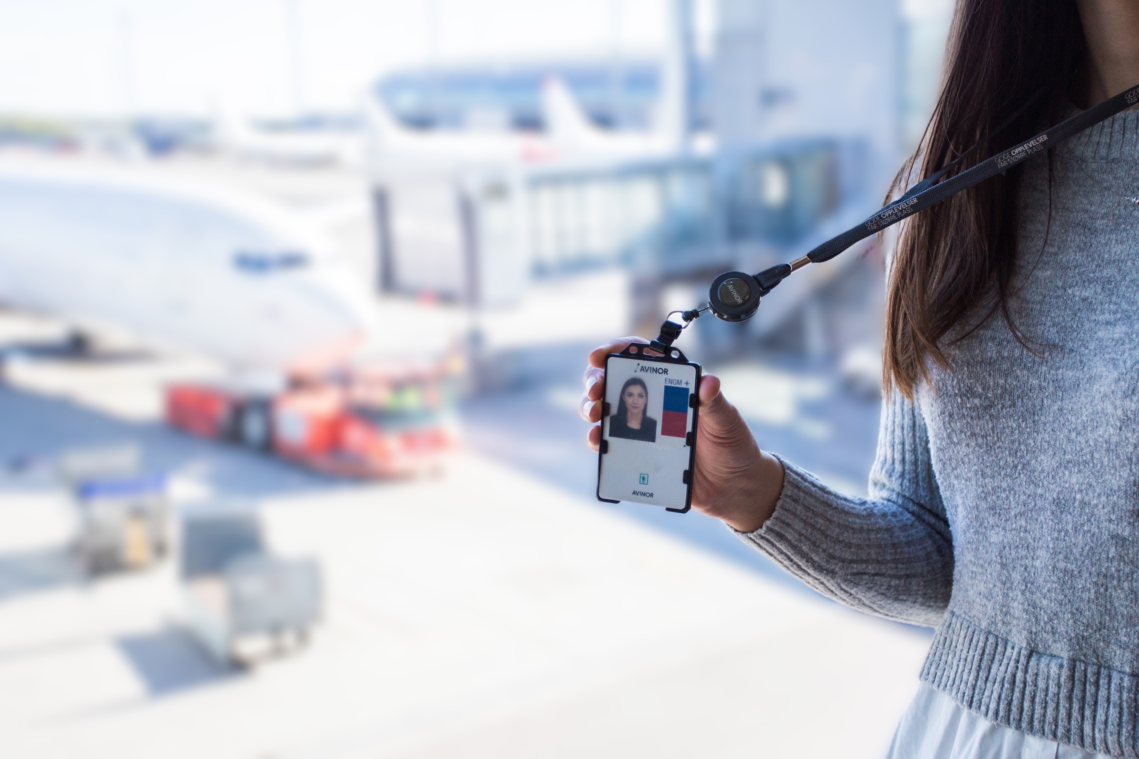 Woman holding employee ID badge in airport terminal with airplane in background
